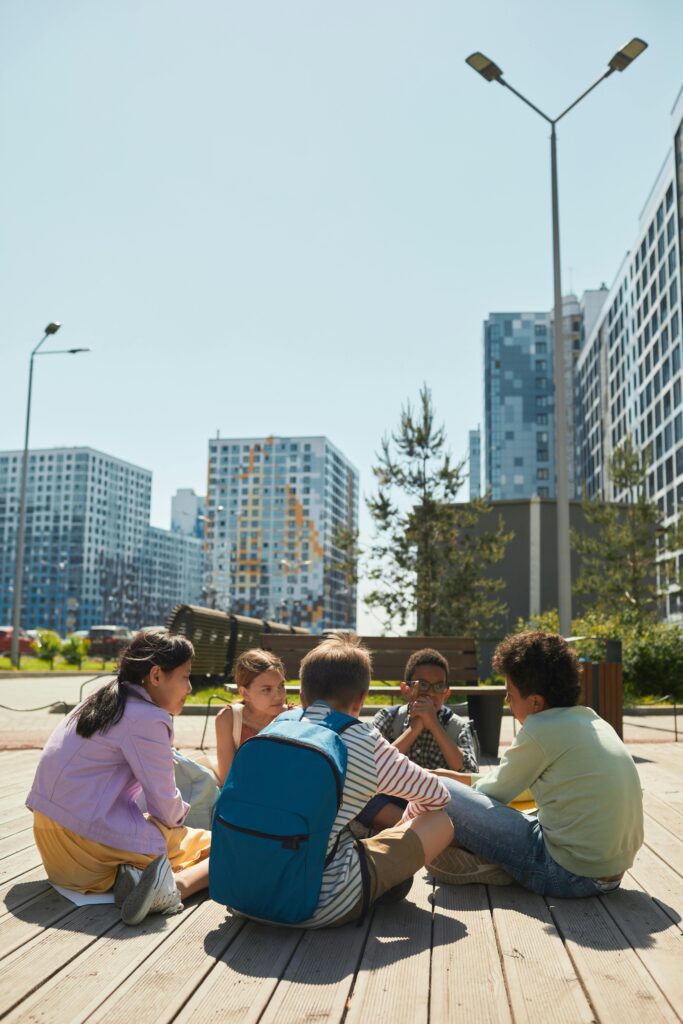 Group of kids sitting in a park surrounded by city skyscrapers during summer day.